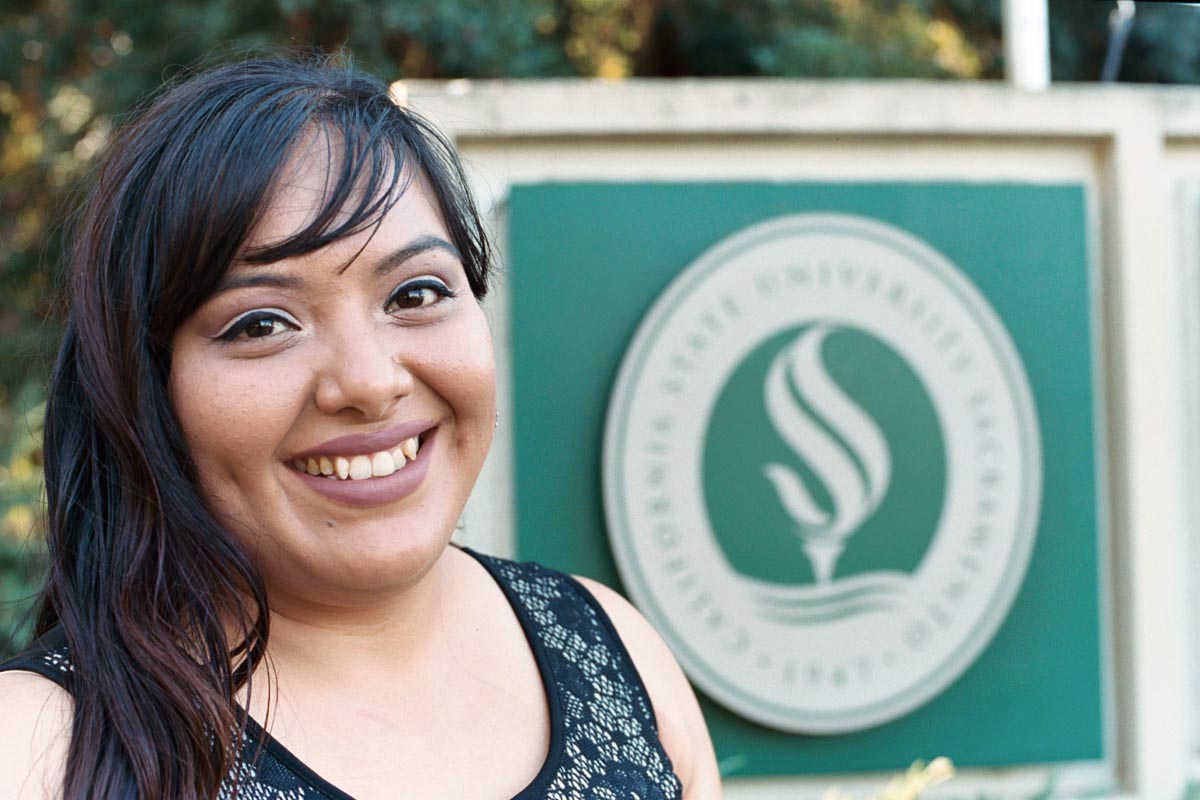 CSUS Graduate stands in front of her Alma Mater crest