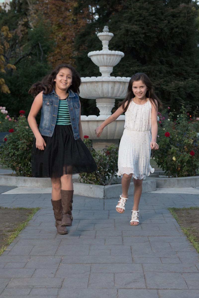 Two sisters skipping long with big smiles in Sacramento's Rose Garden